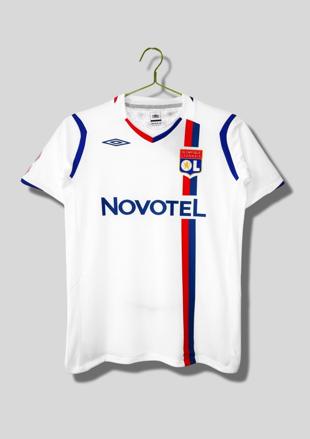 Olympique Lyonnais domicile 2008-2009 : maillot blanc Umbro avec une fine bande verticale bicolore rouge et bleue passant sous le blason, col en V bleu et rouge, sponsor Novotel. GoalKits