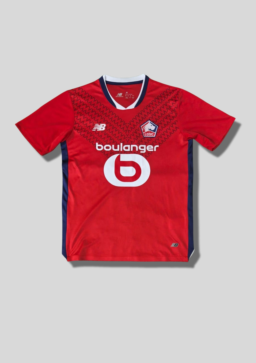LOSC Lille domicile 2024-2025 : maillot rouge avec un motif de chevrons ton sur ton, col en V et bords de manches bleu marine et blanc, logos blancs et sponsor Boulanger. GoalKits