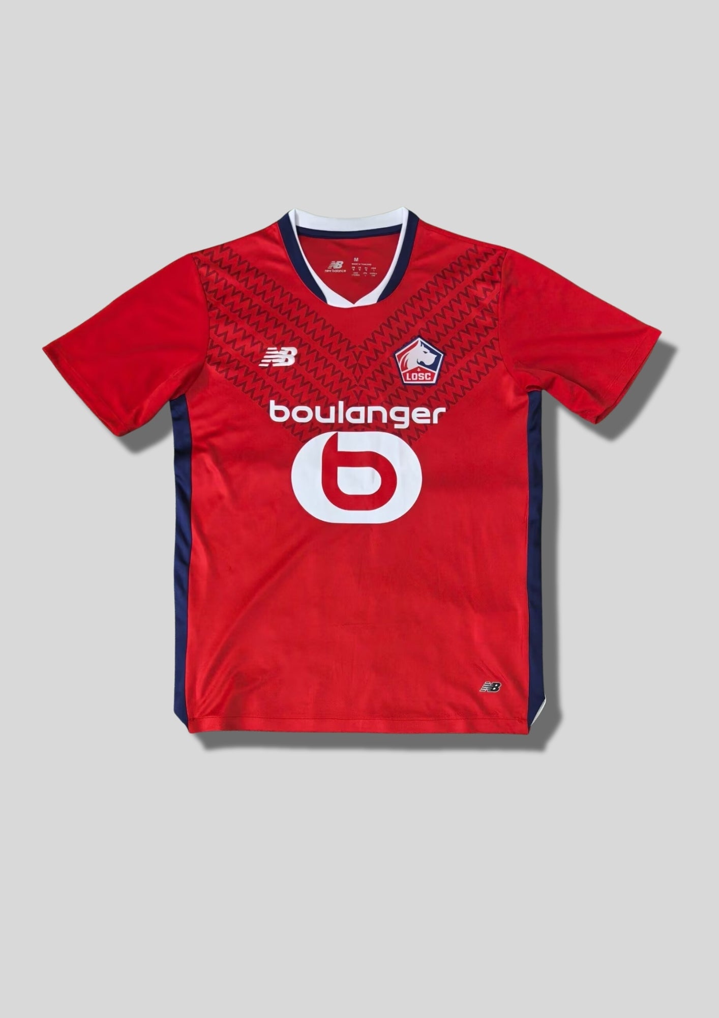 LOSC Lille domicile 2024-2025 : maillot rouge avec un motif de chevrons ton sur ton, col en V et bords de manches bleu marine et blanc, logos blancs et sponsor Boulanger. GoalKits