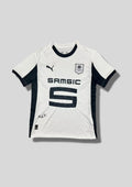 Stade Rennais extérieur 2024-2025 : maillot blanc avec un motif discret de fines lignes en losanges sur le torse, col rond et larges bandes latérales noirs, logos et sponsor Samsic noirs. GoalKits