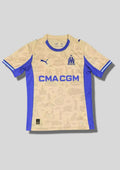Olympique de Marseille "Third" 2024-2025 : maillot couleur sable/ocre orné de croquis de monuments marseillais, avec des panneaux latéraux, un col et des logos bleu roi. GoalKits