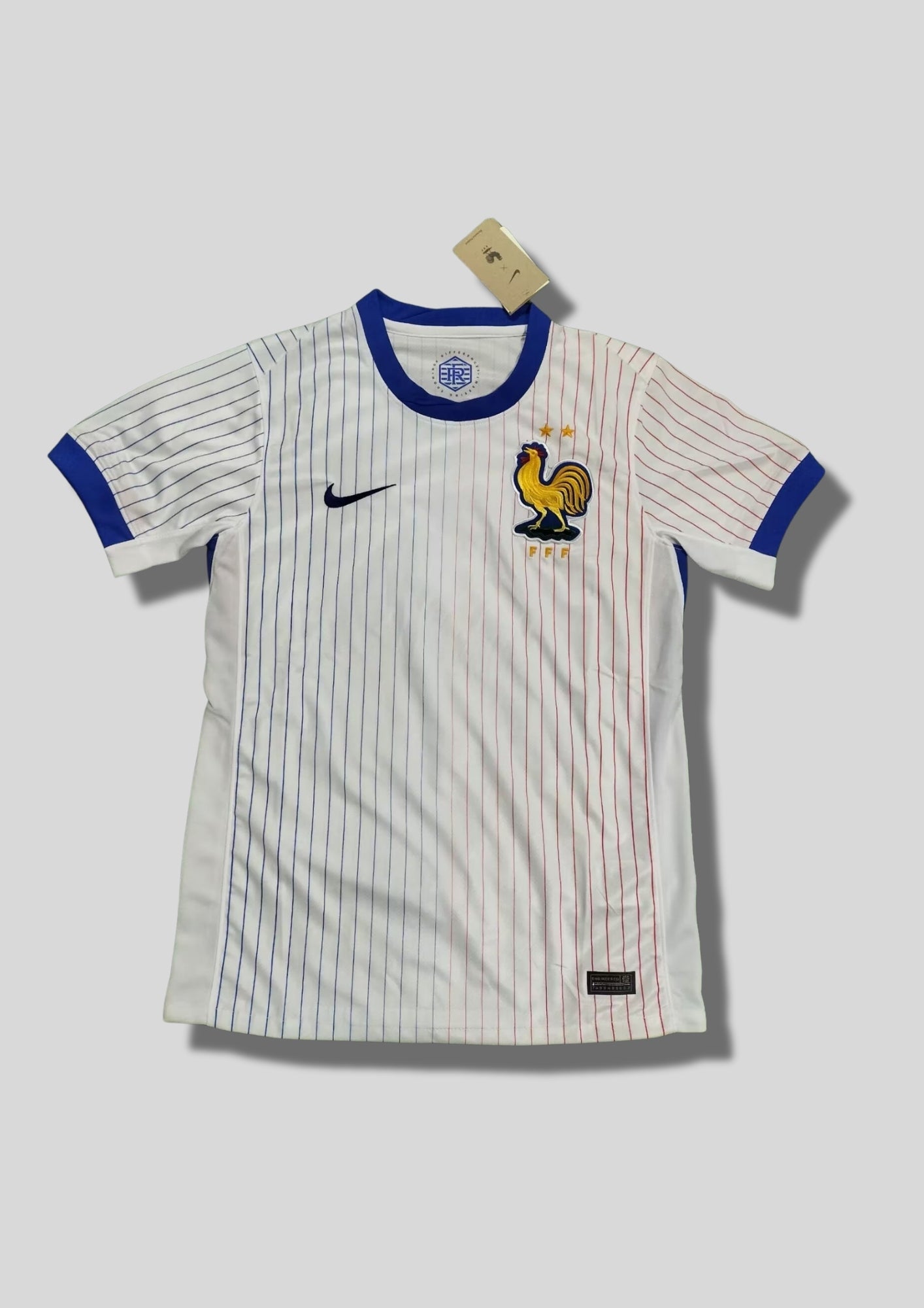 France Extérieur Euro 2024 : Blanc avec fines rayures verticales dégradées bleues et rouges, col et bords de manches bleus, coq géant doré. GoalKits