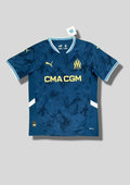 Olympique de Marseille extérieur 2024-2025 : maillot bleu turquoise avec un motif effet "tie-dye" ou fumée sombre, logos et sponsor CMA CGM jaunes, détails blancs sur les flancs. GoalKits
