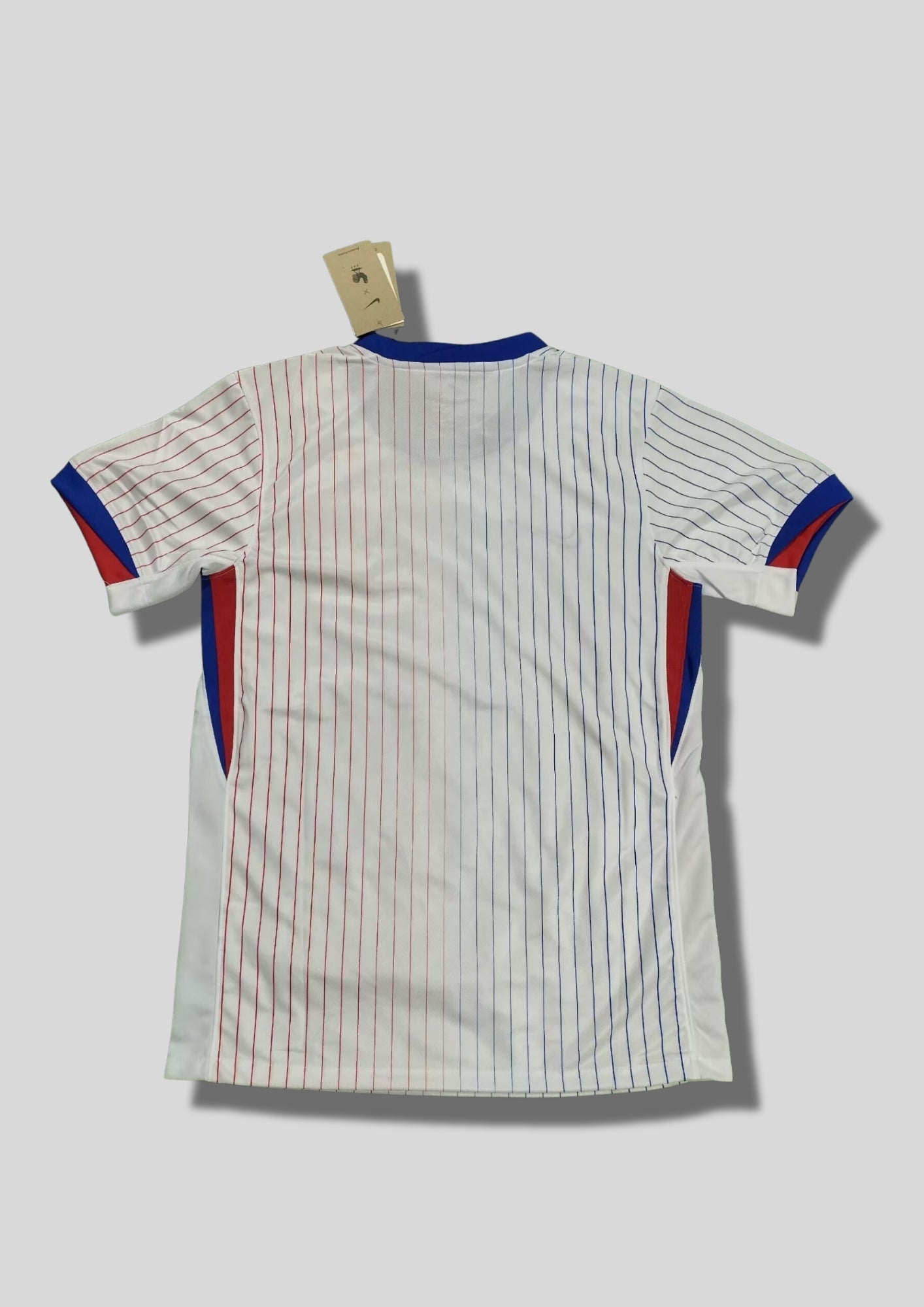 France Extérieur Euro 2024 : Blanc avec fines rayures verticales dégradées bleues et rouges, col et bords de manches bleus, coq géant doré. GoalKits