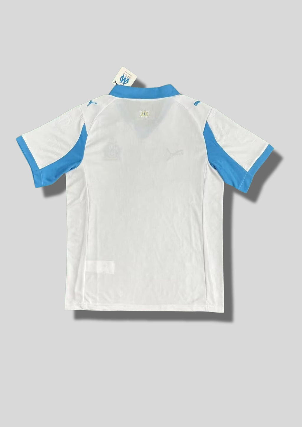 Olympique de Marseille domicile 2024-2025 : maillot blanc avec un col rond et des bords de manches bleu roi, panneaux latéraux décorés de motifs géométriques gris et menthe, blason classique et sponsor CMA CGM bleu. GoalKits