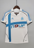 OM domicile 2006-2007 : maillot blanc Adidas avec une large croix bleu ciel asymétrique sur le torse, des liserés noirs incurvés et le sponsor Neuf Telecom. GoalKits