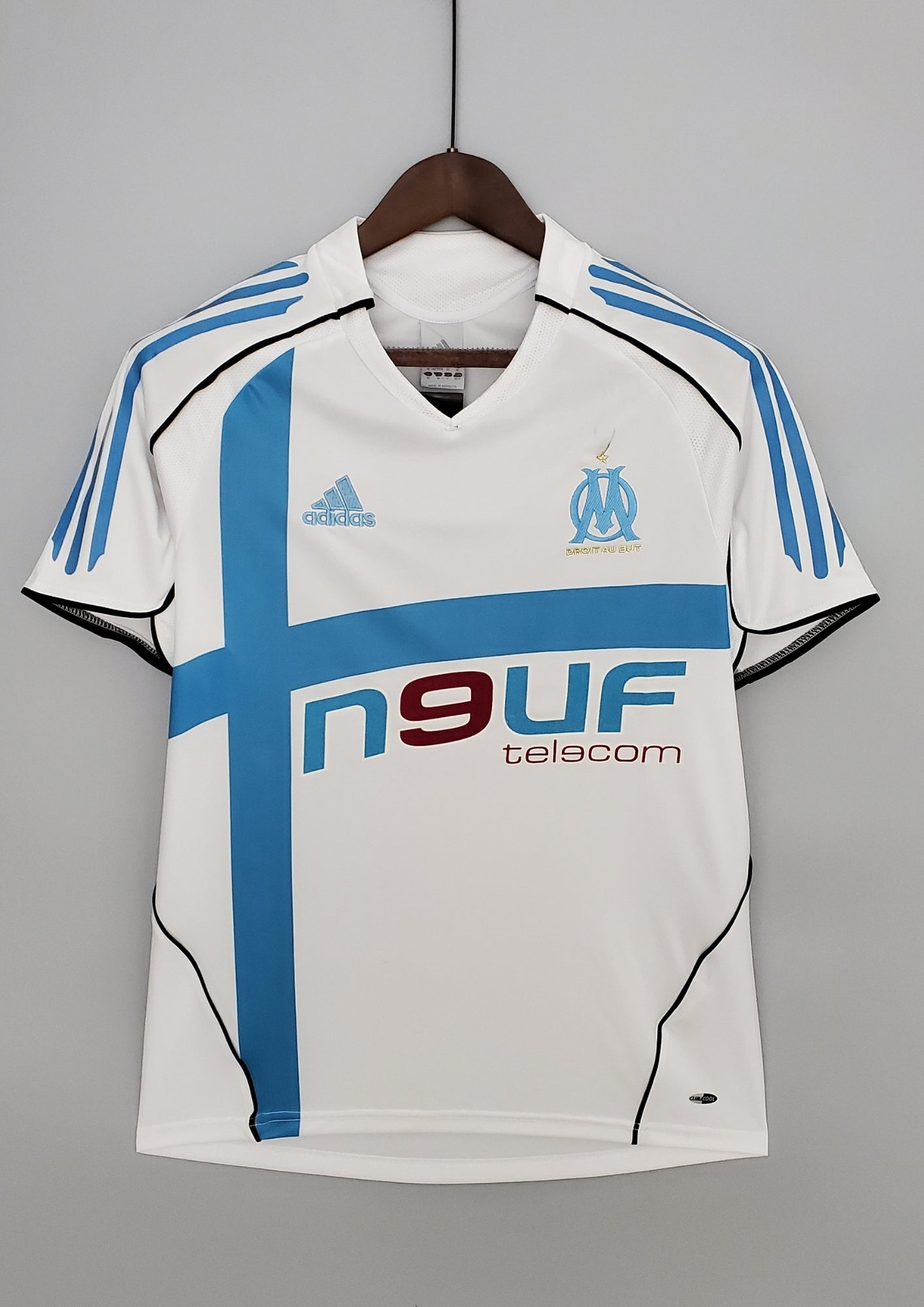 OM domicile 2006-2007 : maillot blanc Adidas avec une large croix bleu ciel asymétrique sur le torse, des liserés noirs incurvés et le sponsor Neuf Telecom. GoalKits