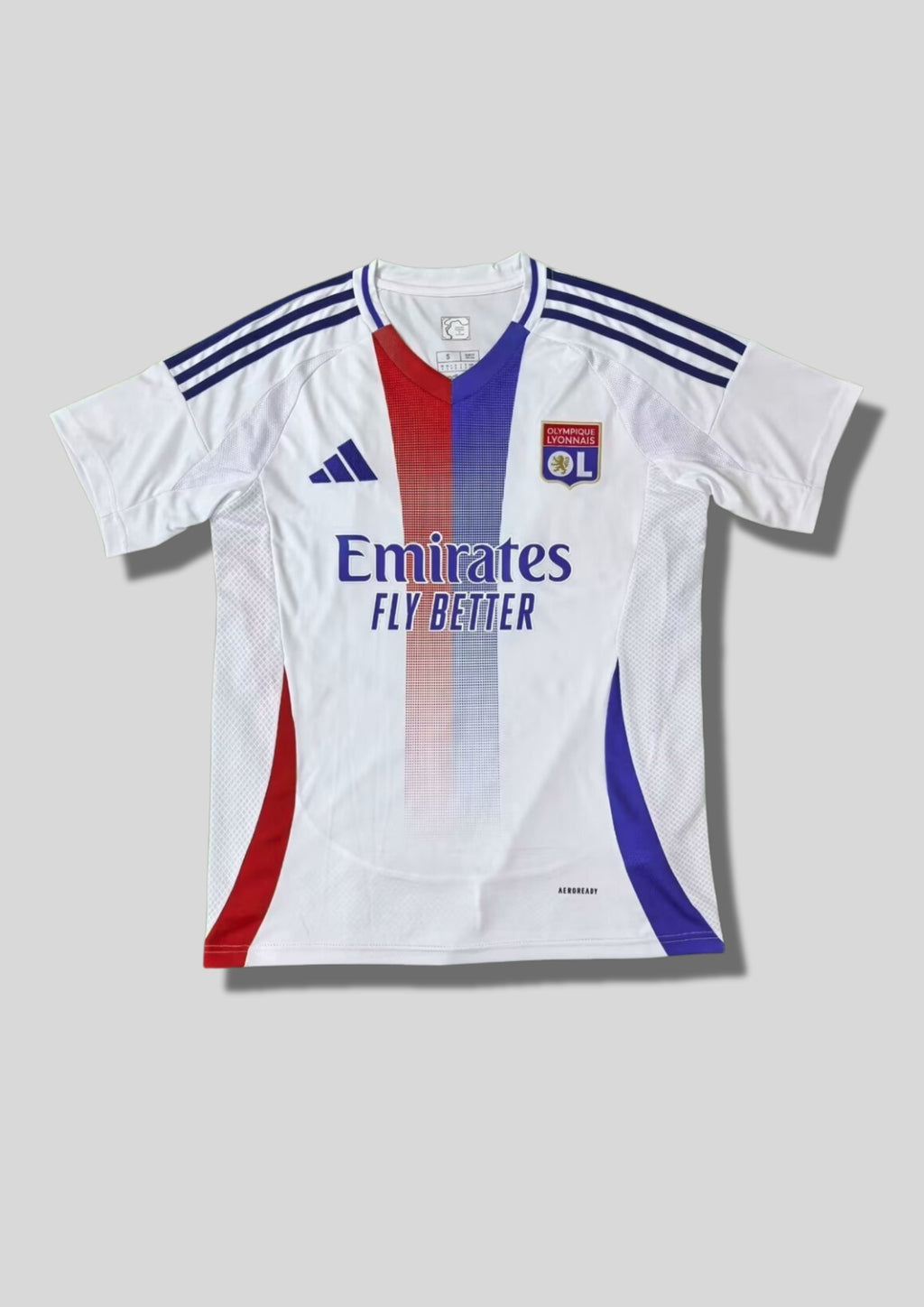 Olympique Lyonnais domicile 2024-2025 : maillot blanc avec deux bandes verticales centrales dégradées rouge et bleue, bandes Adidas bleu marine sur les épaules et sponsor Emirates. GoalKits