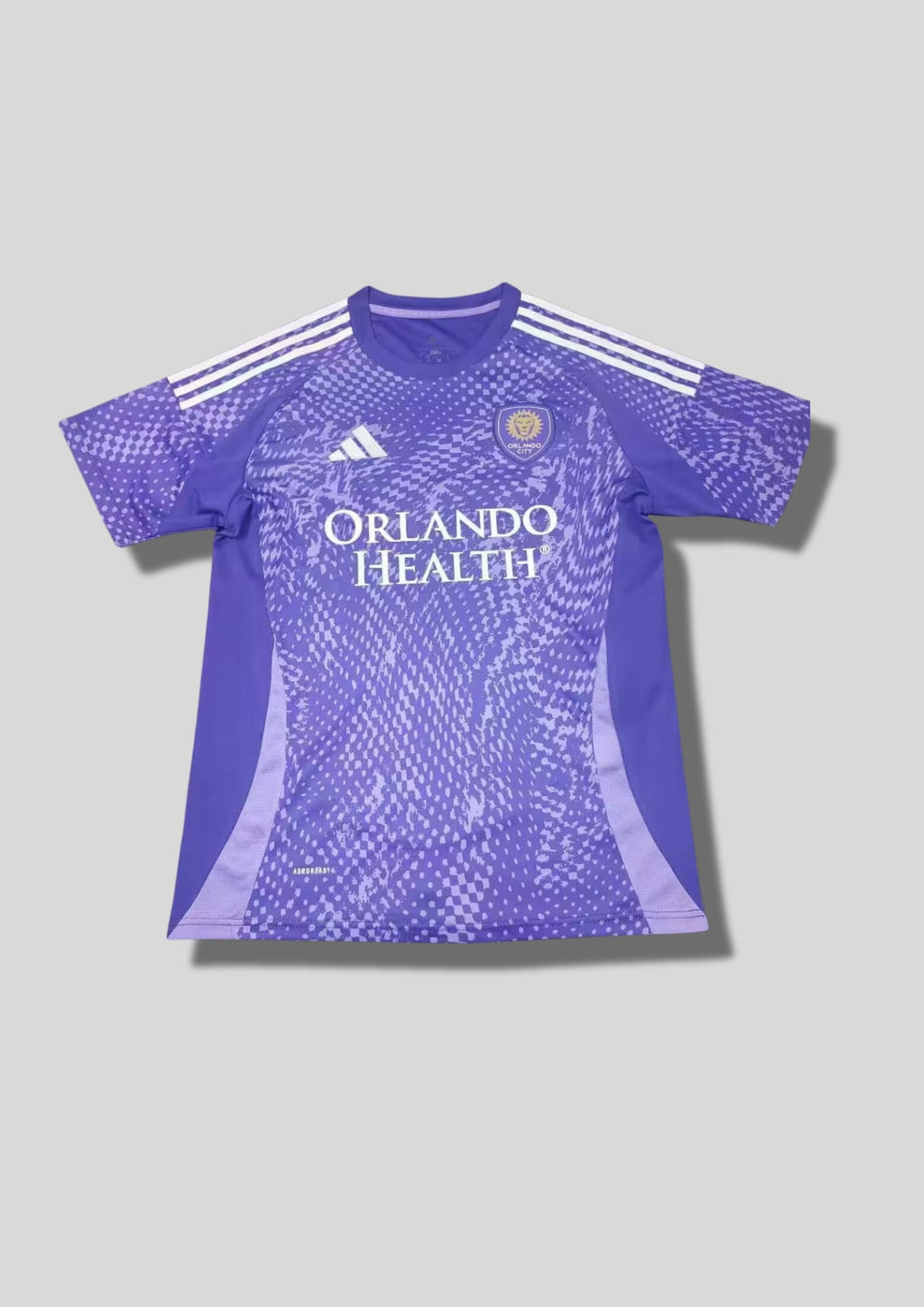 Orlando City SC Pre-Match 24/25 : Violet avec des motifs graphiques texturés en dégradé de pixels et le sponsor "ORLANDO HEALTH". GoalKits