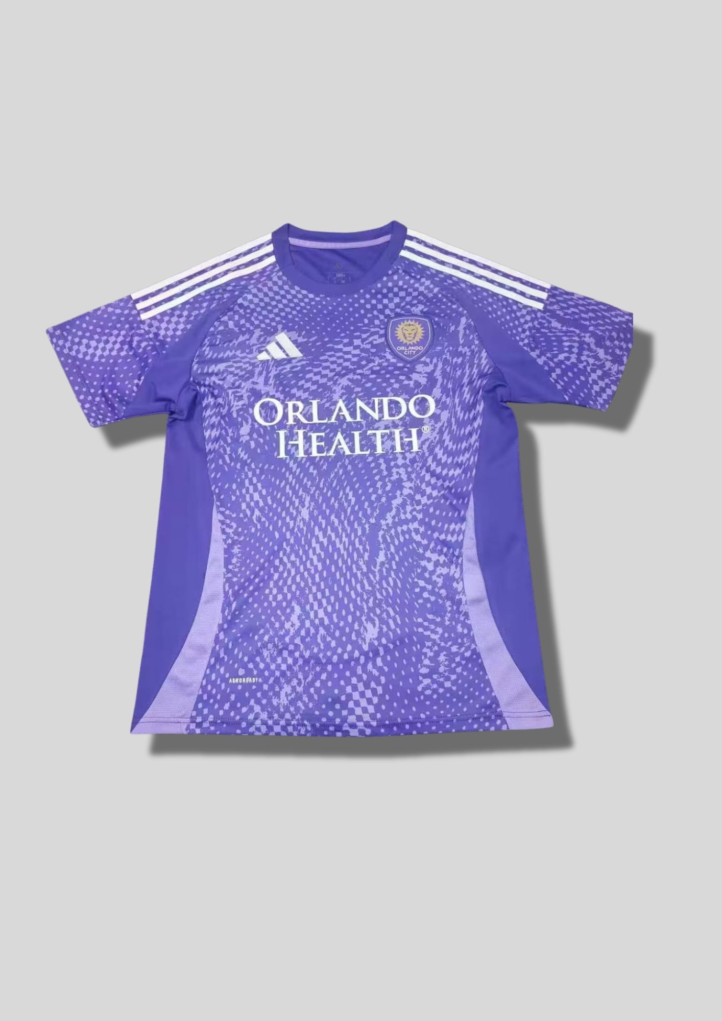 Orlando City SC Pre-Match 24/25 : Violet avec des motifs graphiques texturés en dégradé de pixels et le sponsor "ORLANDO HEALTH". GoalKits