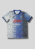 Atalanta Bergame Away 24/25 : Design blanc et bleu avec des motifs en barres verticales pixélisées, logo Joma et sponsors "Lete" et "Radici Group". GoalKits
