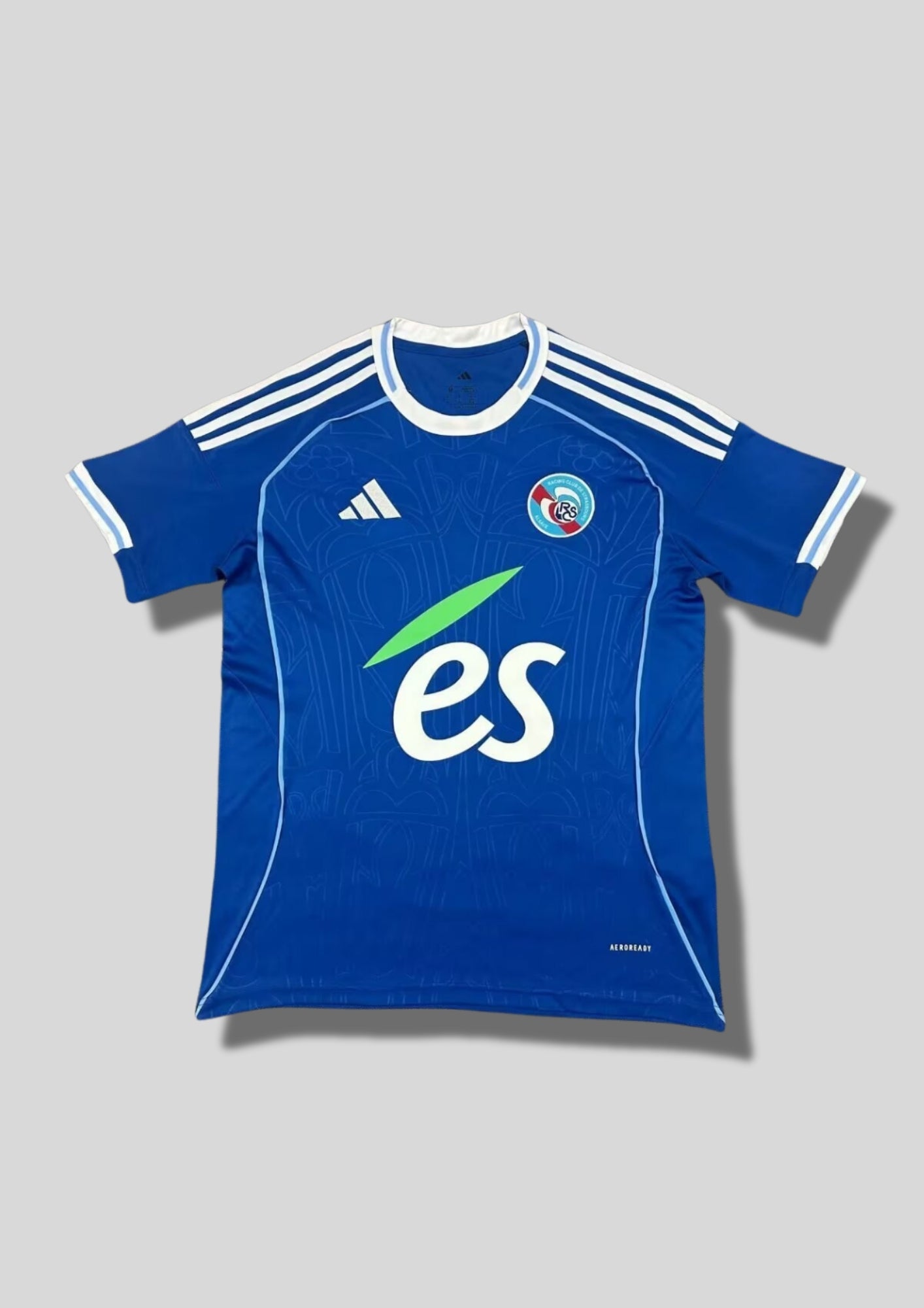 RC Strasbourg domicile 2024-2025 : maillot bleu royal Adidas avec des motifs baroques ton sur ton inspirés de la cathédrale de Strasbourg, col rond blanc et sponsor es. GoalKits