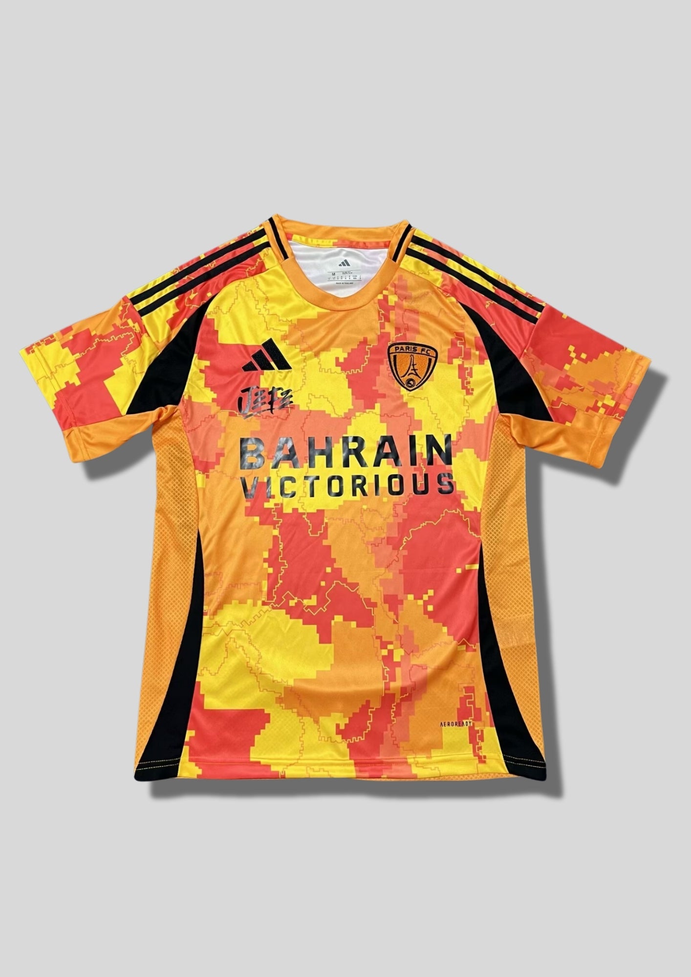 Paris FC "Third" 2024-2025 : maillot Adidas aux couleurs vives (orange, jaune et rouge) avec un motif camouflage pixelisé représentant les arrondissements de Paris, logos noirs et sponsor Bahrain Victorious. GoalKits