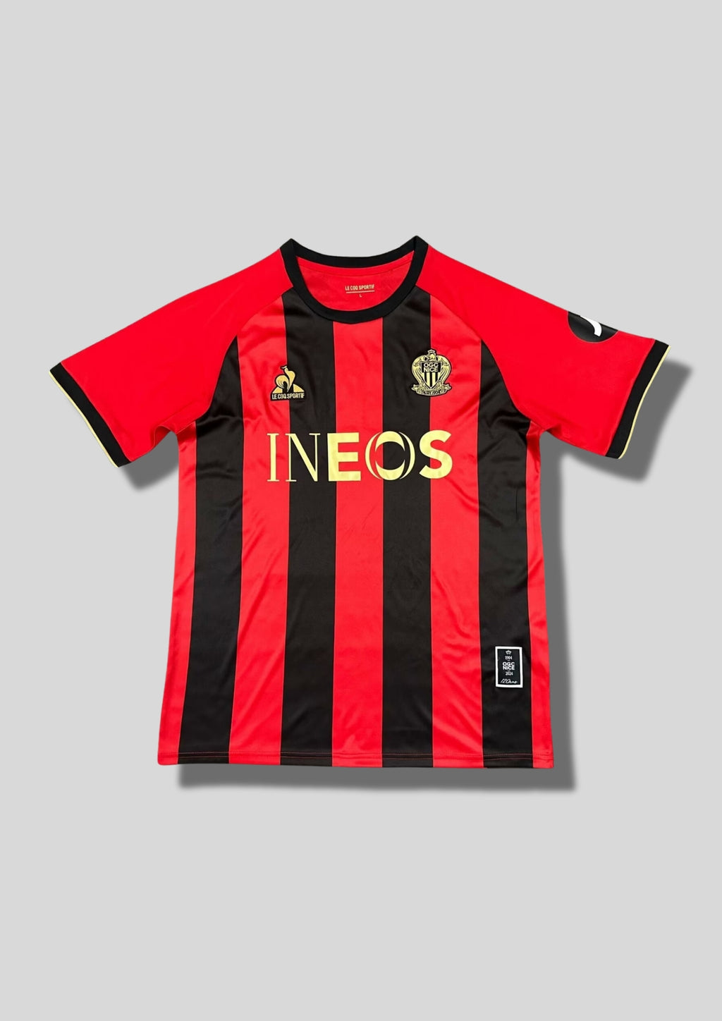 OGC Nice domicile 2024-2025 (120 ans) : maillot Le Coq Sportif aux rayures verticales rouges et noires traditionnelles, avec des logos et le sponsor INEOS dorés pour célébrer l'anniversaire du club. GoalKits