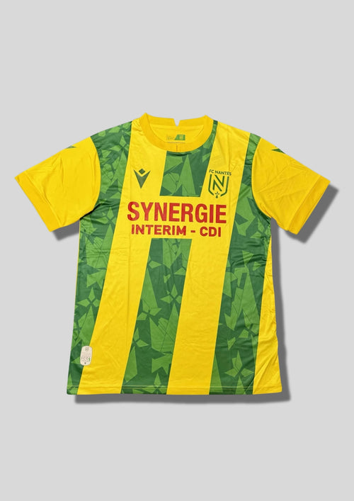 C Nantes extérieur 2024-2025 : maillot Macron présentant de larges bandes verticales jaunes et vertes, ces dernières étant ornées de motifs géométriques ton sur ton, avec le sponsor SYNERGIE en rouge. GoalKits