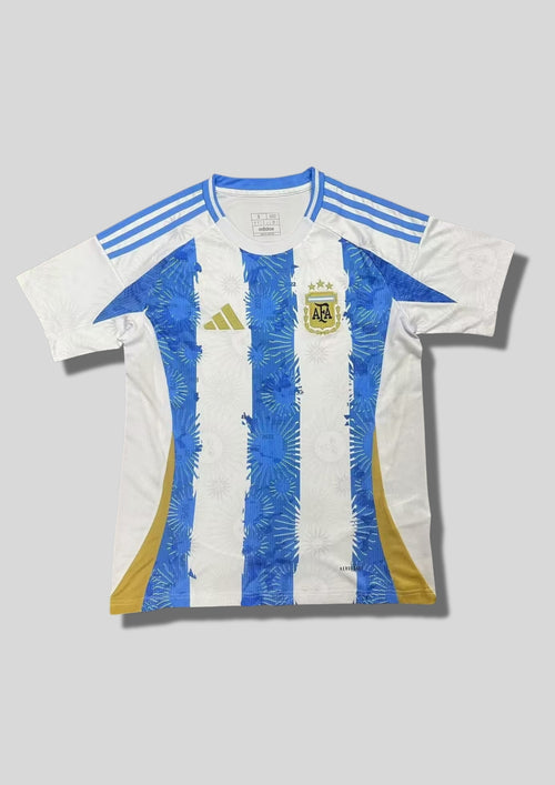 Argentine 2024 (Pre-Match) Blanc et ciel, rayures verticales graphiques avec motifs de soleils et d'étoiles, détails dorés sur les flancs. GoalKits