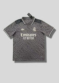 Real Madrid : Maillot d'entraînement / Édition Spéciale – Gris anthracite avec un motif monogramme intégral de lettres entrelacées, col polo boutonné et logos blancs. GoalKits