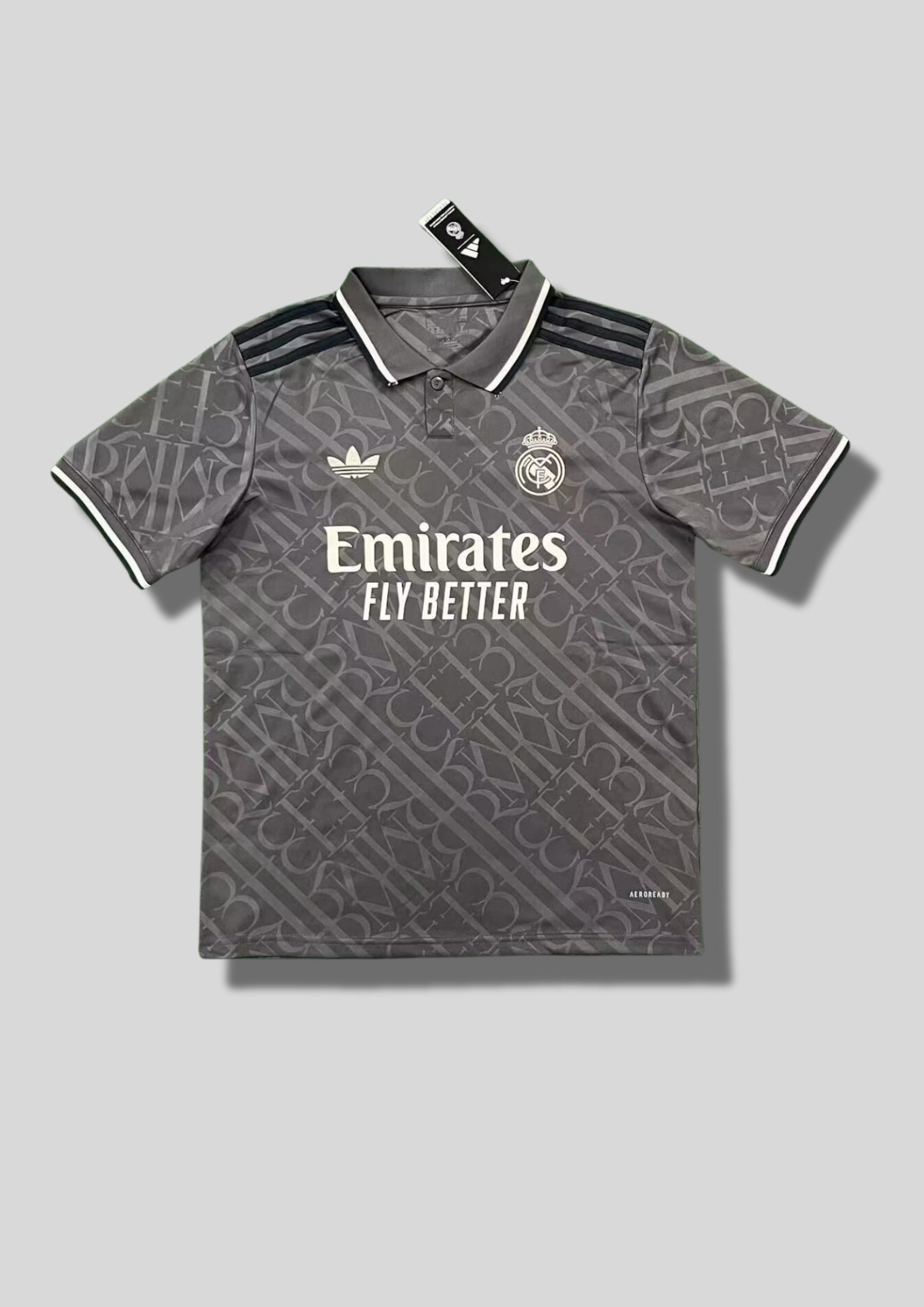 Real Madrid : Maillot d'entraînement / Édition Spéciale – Gris anthracite avec un motif monogramme intégral de lettres entrelacées, col polo boutonné et logos blancs. GoalKits