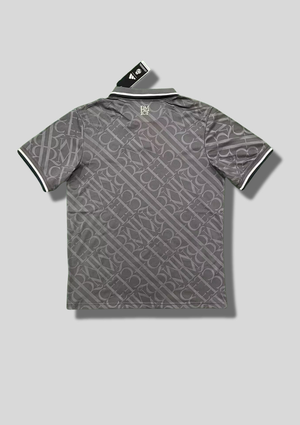 Real Madrid : Maillot d'entraînement / Édition Spéciale – Gris anthracite avec un motif monogramme intégral de lettres entrelacées, col polo boutonné et logos blancs. GoalKits