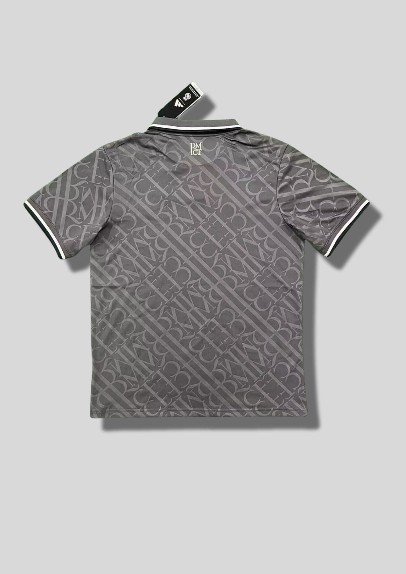 Real Madrid : Maillot d'entraînement / Édition Spéciale – Gris anthracite avec un motif monogramme intégral de lettres entrelacées, col polo boutonné et logos blancs. GoalKits