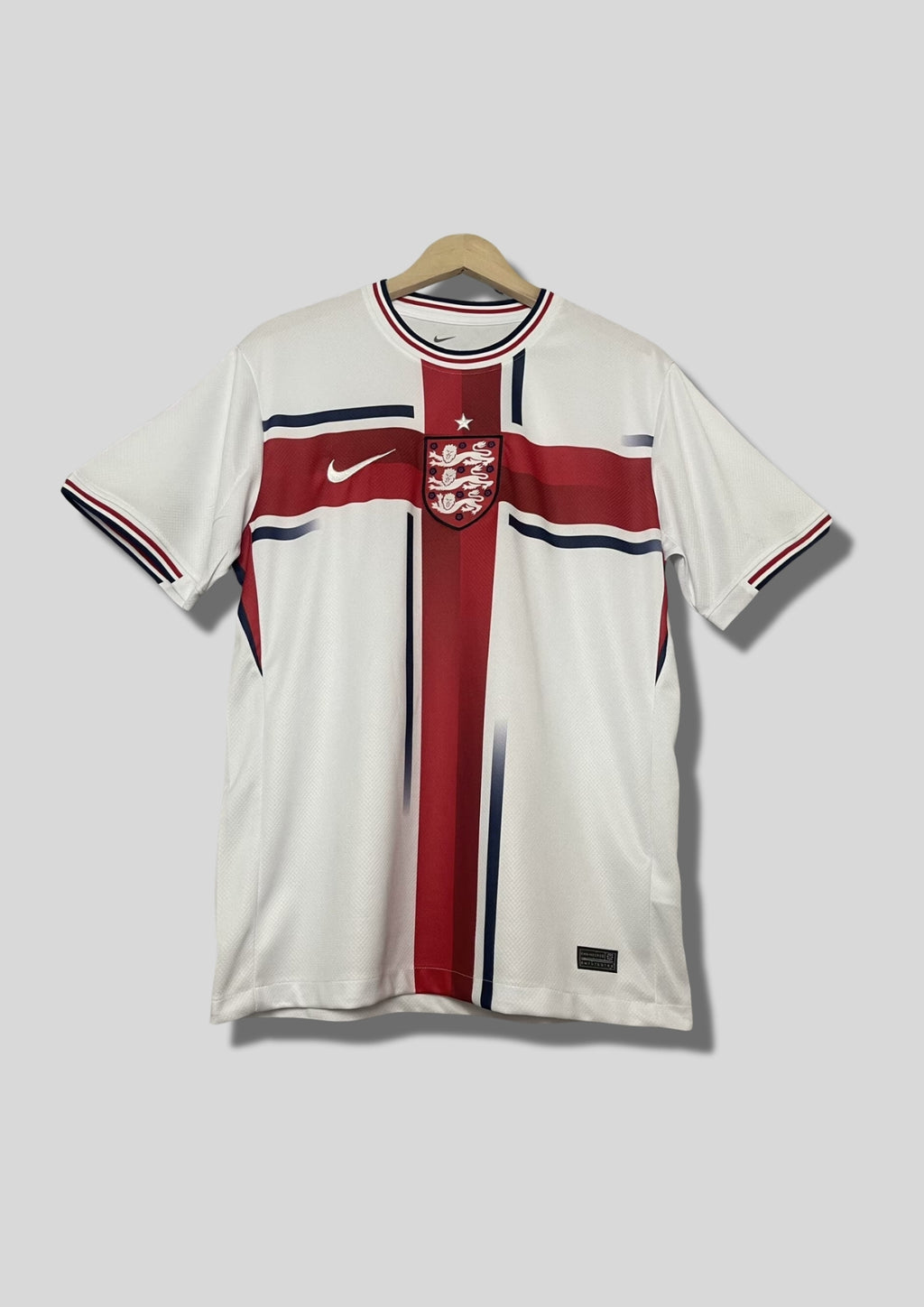 Angleterre 2024 (Concept/Cross) Blanc avec une large croix de Saint-Georges rouge centrée, bordée de fines lignes bleu marine. Le logo Nike et l'écusson des Three Lions sont placés de part et d'autre de la croix. GoalKits