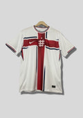 Angleterre 2024 (Concept/Cross) Blanc avec une large croix de Saint-Georges rouge centrée, bordée de fines lignes bleu marine. Le logo Nike et l'écusson des Three Lions sont placés de part et d'autre de la croix. GoalKits