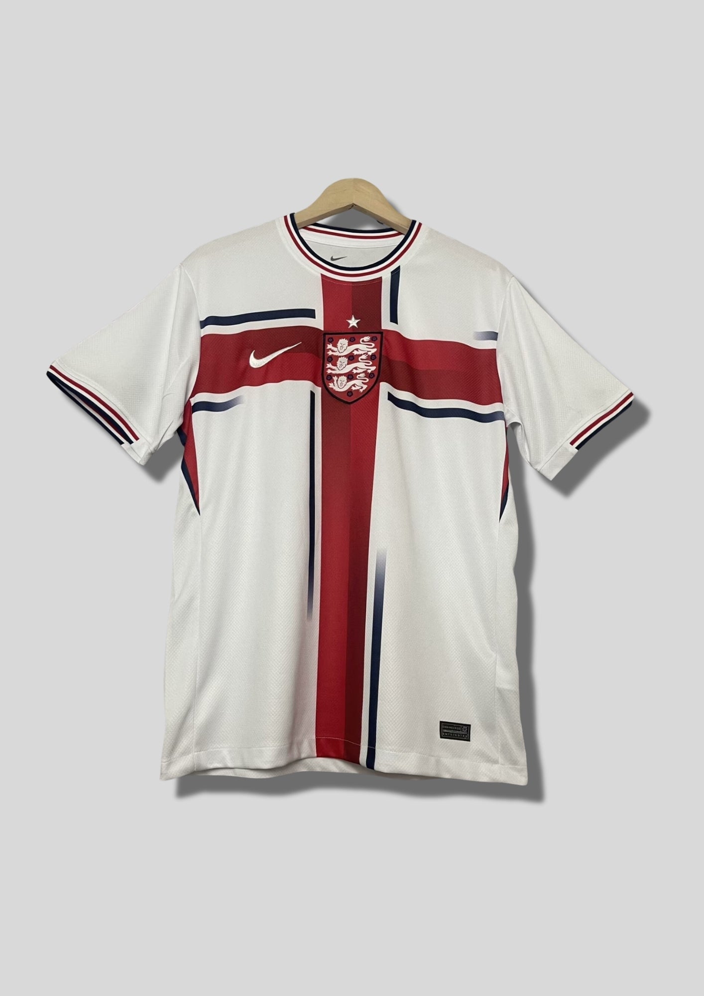 Angleterre 2024 (Concept/Cross) Blanc avec une large croix de Saint-Georges rouge centrée, bordée de fines lignes bleu marine. Le logo Nike et l'écusson des Three Lions sont placés de part et d'autre de la croix. GoalKits