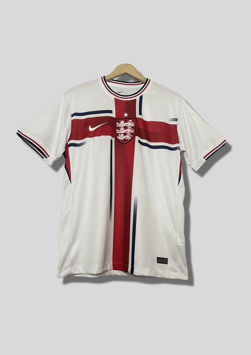 Angleterre 2024 (Concept/Cross) Blanc avec une large croix de Saint-Georges rouge centrée, bordée de fines lignes bleu marine. Le logo Nike et l'écusson des Three Lions sont placés de part et d'autre de la croix. GoalKits