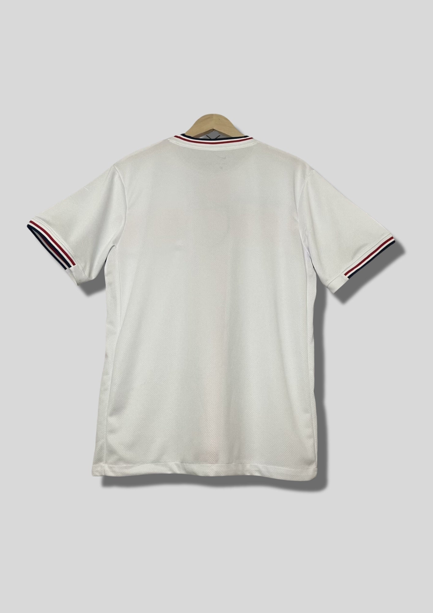 Angleterre 2024 (Concept/Cross) Blanc avec une large croix de Saint-Georges rouge centrée, bordée de fines lignes bleu marine. Le logo Nike et l'écusson des Three Lions sont placés de part et d'autre de la croix. GoalKits